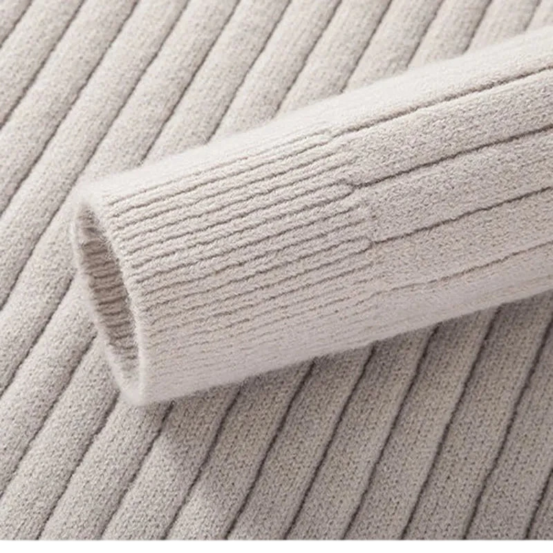 Zbliżenie na beżowy sweter męski Arkadya Outlet z półzamkiem, dopasowanym krojem, kołnierzem stojącym i długim rękawem pokazuje jego prążkowany rękaw na dopasowanym materiale, podkreślając jego smukłą fakturę i szczegółowy wzór.