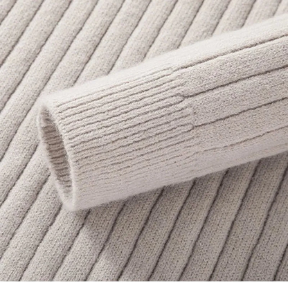 Zbliżenie na beżowy sweter męski Arkadya Outlet z półzamkiem, dopasowanym krojem, kołnierzem stojącym i długim rękawem pokazuje jego prążkowany rękaw na dopasowanym materiale, podkreślając jego smukłą fakturę i szczegółowy wzór.