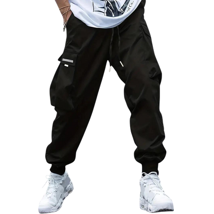 Model noszący Arkadya Outlet Męskie spodnie cargo z dopasowaną nogawką i wieloma kieszeniami, czarne, zestawione z białymi sneakersami. Widoczna tylko dolna część sylwetki na jasnoszarym tle.