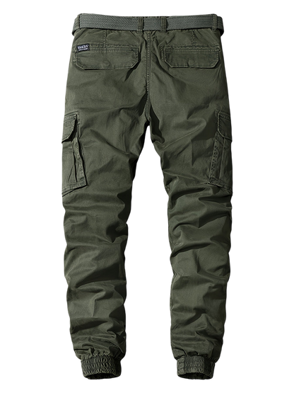 Arkadya Outlet Męskie Spodnie joggery w oliwkowym kolorze z elastycznymi mankietami, dwoma kieszeniami z tyłu z klapkami i bocznymi kieszeniami cargo. Casualowy, wytrzymały styl na szarym tle gradientowym.