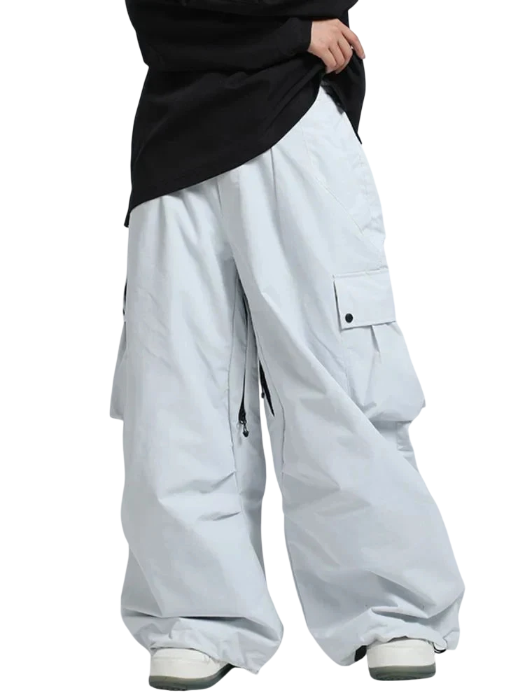 Osoba ubrana w ponadgabarytowe Arkadya Outlet Spodnie zimowe męskie szeroki krój regularny, z dużymi kieszeniami cargo, luźną czarną koszulą i białymi trampkami na jasnoszarym tle. Te zimowe spodnie są idealne na zimę i dotykają ziemi.