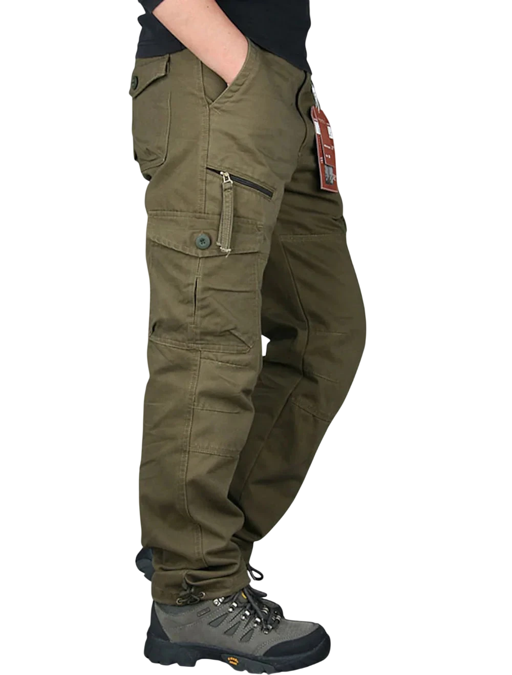Osoba ma na sobie Arkadya Outlet Spodnie cargo męskie prosta nogawka z kieszeniami i zamkiem oraz szare buty turystyczne, stoi z jedną ręką w kieszeni. Spodnie mają wiele kieszeni, zamki błyskawiczne, metkę na szlufce, na białym tle.