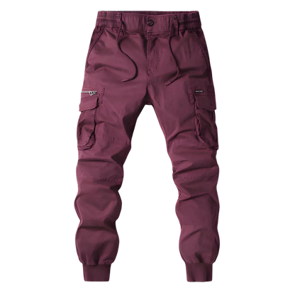 Arkadya Outlet Spodnie Cargo Męskie Kieszenie Na Zamek - bordowe joggery z elastycznym pasem, sznurkiem ściągającym, kieszeniami zapinanymi na zamek i mankietami na kostkach, pokazane na rozmytym tle miasta.