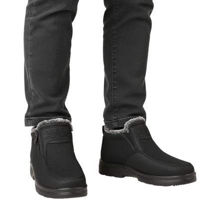 Osoba ubrana w Arkadya Outlet Męskie buty wodoodporne antypoślizgowe zimowe obuwie z bocznymi zamkami, futrzaną podszewką i ciemnymi dżinsami stoi na jasnym tle. Buty mają antypoślizgowe podeszwy i wyglądają na ciepłe i wygodne.