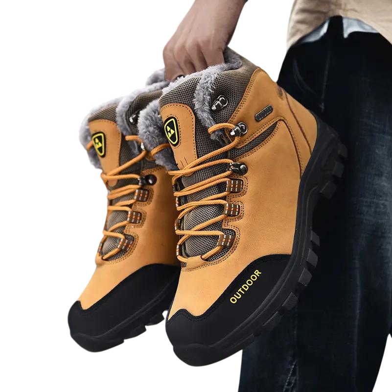 Osoba trzyma Arkadya Outlet Buty zimowe outdoor męskie wiązane z antypoślizgową podeszwą w kolorze opalenizny i czerni z wytrzymałymi bieżnikami, szarą wyściełaną podszewką, żółtymi akcentami, napisem OUTDOOR z boku i solidnymi sznurowadłami.