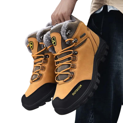 Osoba trzyma Arkadya Outlet Buty zimowe outdoor męskie wiązane z antypoślizgową podeszwą w kolorze opalenizny i czerni z wytrzymałymi bieżnikami, szarą wyściełaną podszewką, żółtymi akcentami, napisem OUTDOOR z boku i solidnymi sznurowadłami.