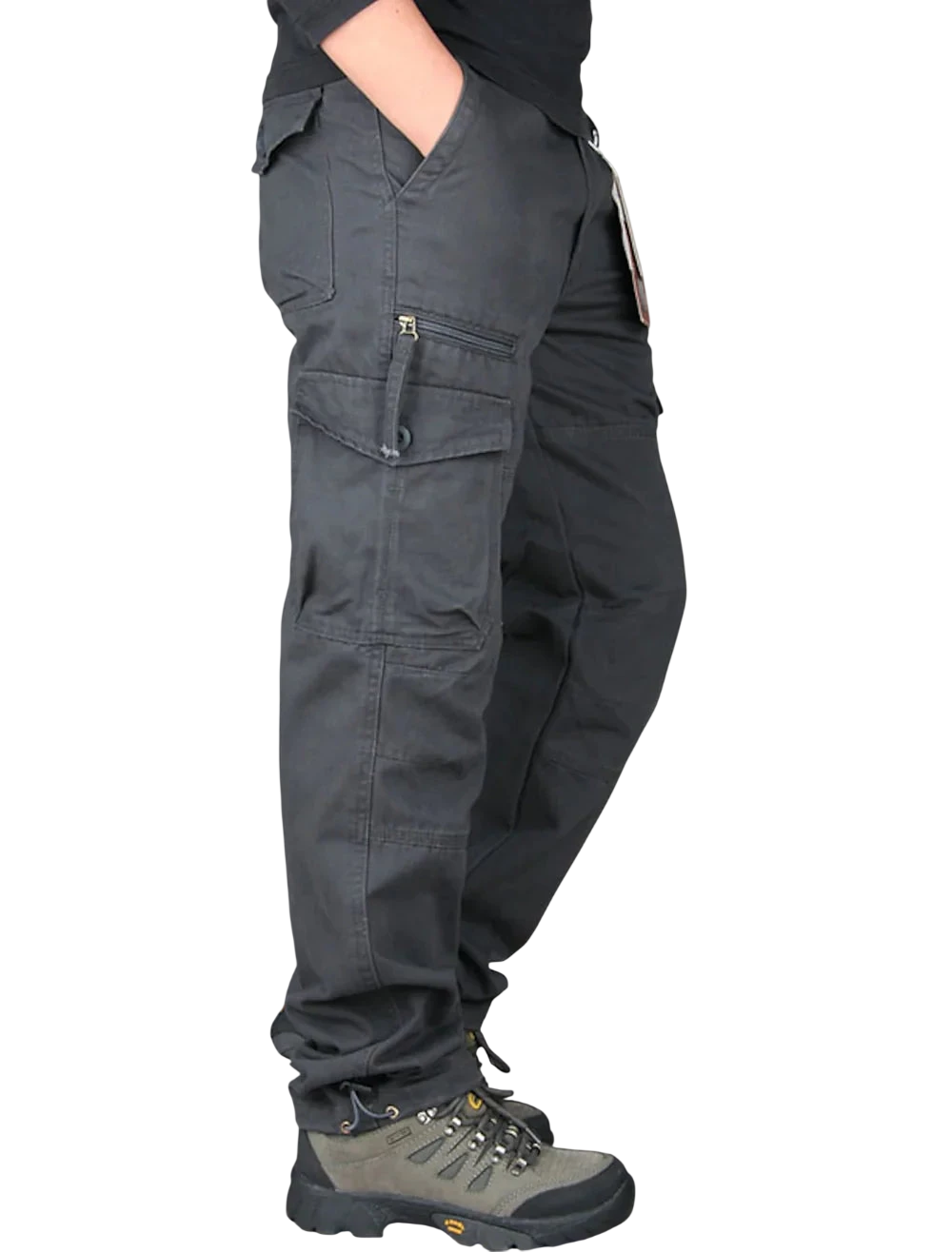 Mężczyzna ubrany w Arkadya Outlet Spodnie cargo męskie prosta nogawka z kieszeniami i zamkiem oraz szare buty turystyczne stoi bokiem z jedną ręką w kieszeni na jasnym tle.