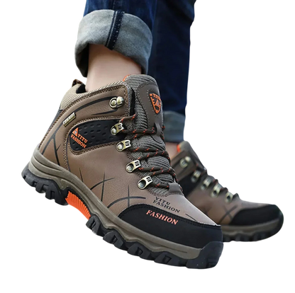 Osoba w męskie buty wodoodporna konstrukcja ergonomiczna podeszwa Arkadya Outlet z pomarańczowymi detalami wchodzi na skałę na zewnątrz, dżinsy podwinięte za kostki i rozmyte drzewa w tle.