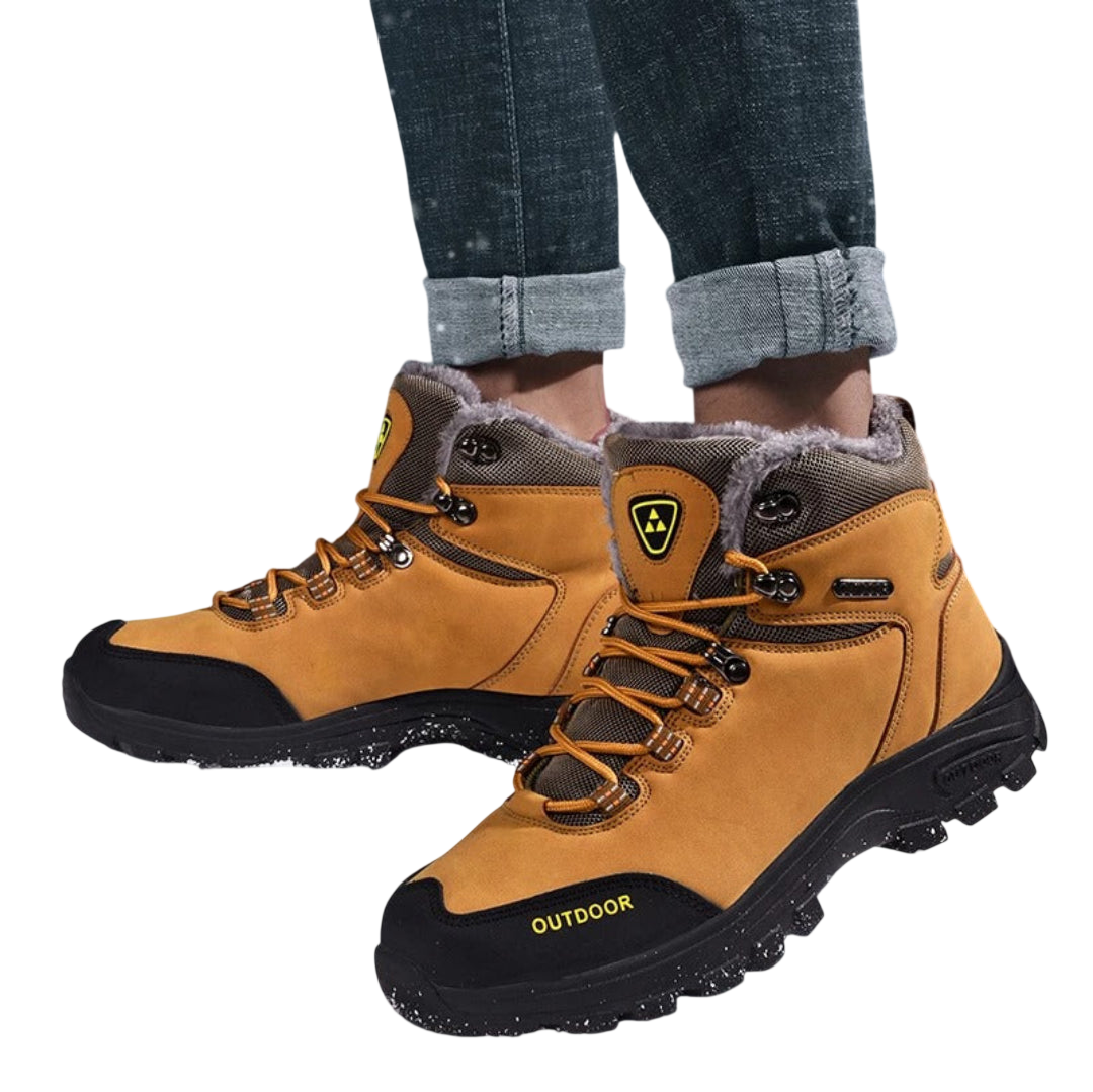 Mężczyzna nosi Buty zimowe outdoor męskie wiązane z antypoślizgową podeszwą Arkadya Outlet w kolorze brązowym i czarnym, z futrzaną podszewką, chropowatą podeszwą, bocznym logo; stylowo łączą się z podwiniętymi dżinsami powyżej kostek.