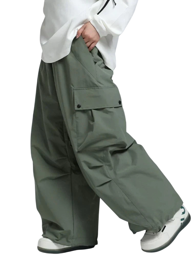 Osoba ubrana w Arkadya Outlet Spodnie zimowe męskie szeroki krój regularny na warunki zimowe, białe trampki i biały top trzyma za sobą deskę snowboardową; widoczna jest tylko jej dolna połowa.