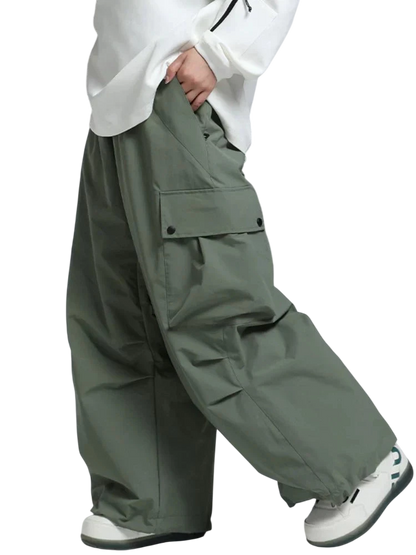 Osoba ubrana w Arkadya Outlet Spodnie zimowe męskie szeroki krój regularny na warunki zimowe, białe trampki i biały top trzyma za sobą deskę snowboardową; widoczna jest tylko jej dolna połowa.