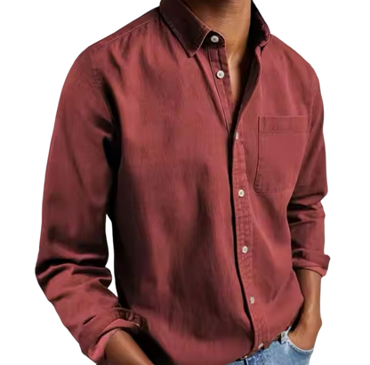 Osoba w Arkadya Outlet Koszula męska klasyczny krój proste linie regularna długość, bordowy z kieszenią na piersi, w połączeniu z jasnoniebieskimi dżinsami, stoi z rękami w kieszeniach na jednolitym tle.