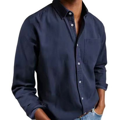 Osoba nosząca Arkadya Outlet Koszula męska klasyczny krój proste linie regularna długość w kolorze ciemnoniebieskim z długimi rękawami i jasnoniebieskimi dżinsami, ręce w kieszeniach, stoi na jednolitym jasnym tle.