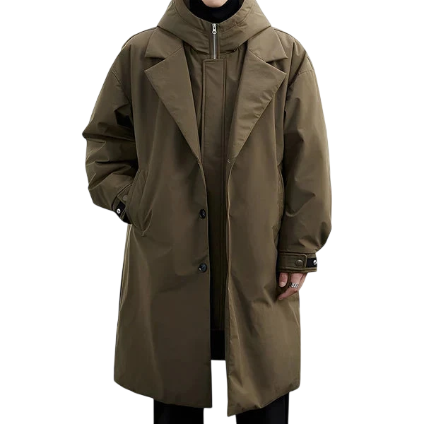 Płaszcz męski wodoodporny długi krój z kapturem podszewką marki Arkadya Outlet na kurtkę z wysokim kołnierzem, stojący na tle białej ściany i szarej podłogi. Oversizowy płaszcz w kolorze oliwkowej zieleni zapewnia styl i wygodę.