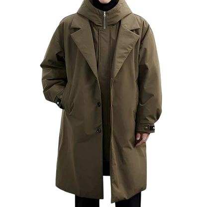 Płaszcz męski wodoodporny długi krój z kapturem podszewką marki Arkadya Outlet na kurtkę z wysokim kołnierzem, stojący na tle białej ściany i szarej podłogi. Oversizowy płaszcz w kolorze oliwkowej zieleni zapewnia styl i wygodę.